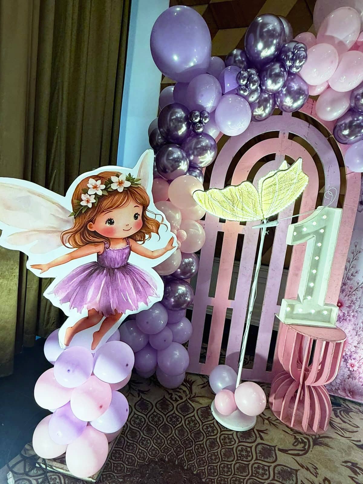 A blush and lilac balloon arch with a fairy cut-out and floral accents